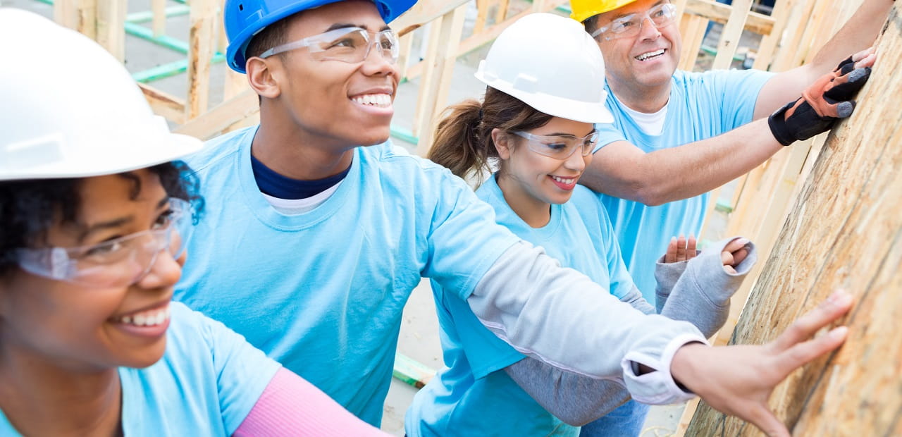 Group of four volunteers in hard hats put the frame of a building together.