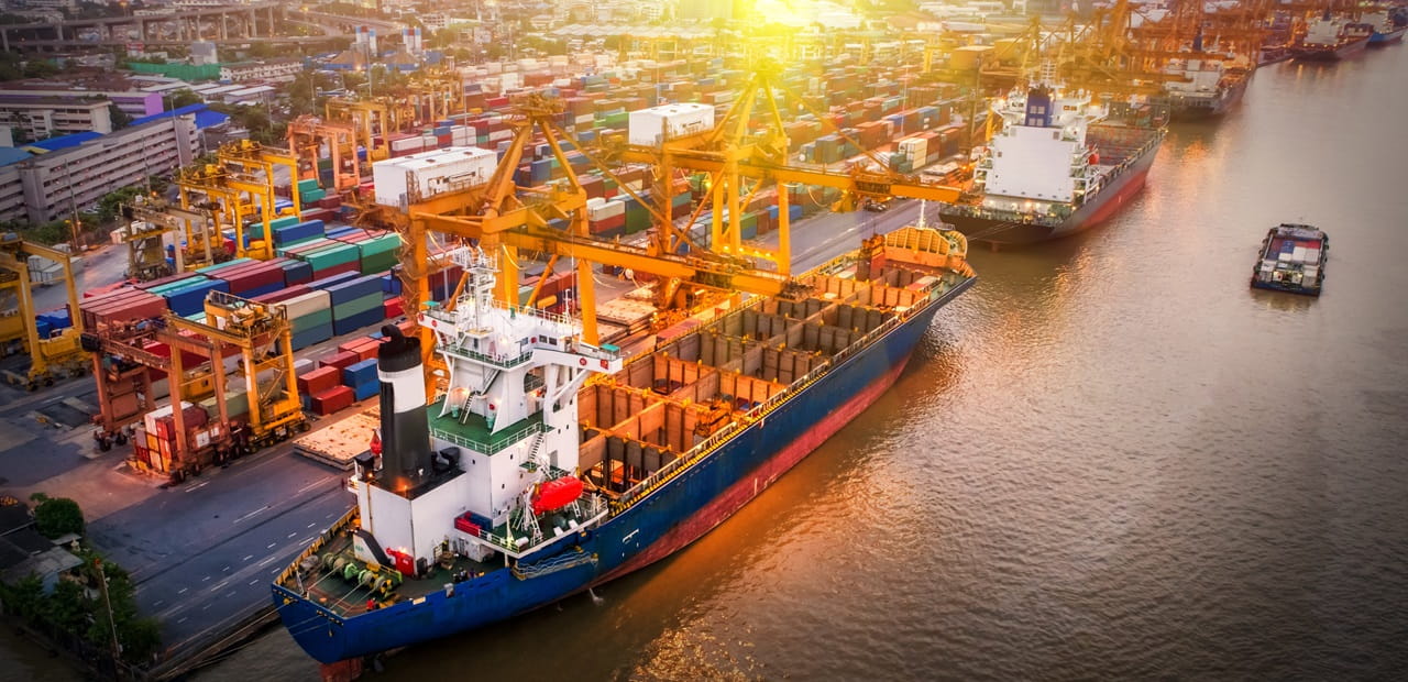 Cargo ship sits in body of water with containers off to the left side on land