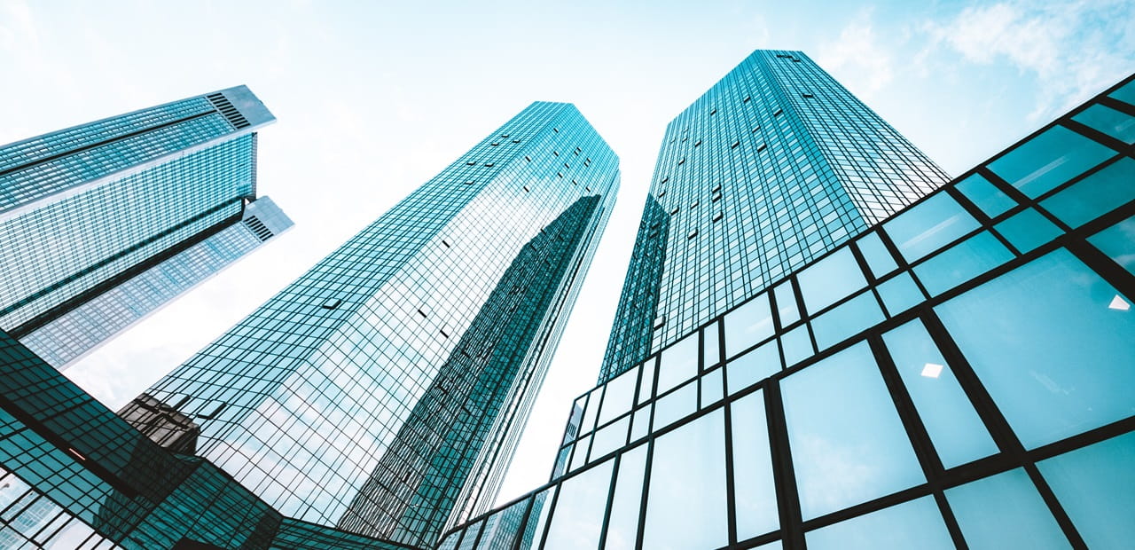 	Low wide-angle view looking up to modern skyscrapers in business district on a beautiful sunny day with blue sky and clouds