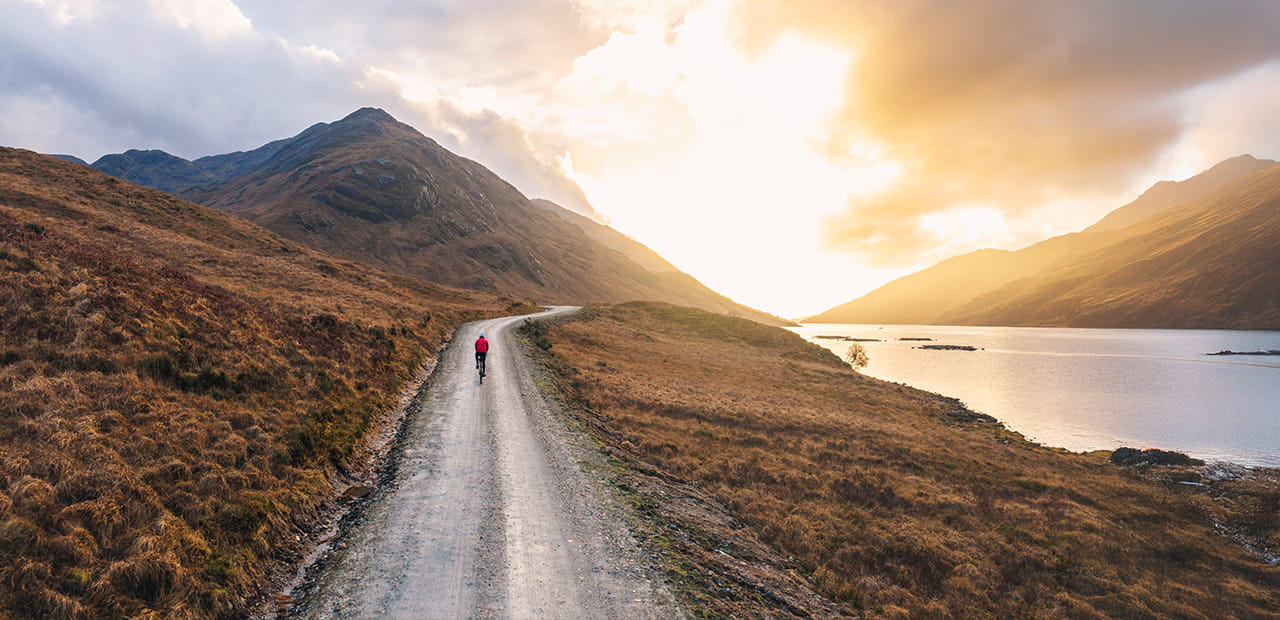Person biking along a winding road at sunrise, symbolizing a mid-year financial check-in and progress toward long-term goals.