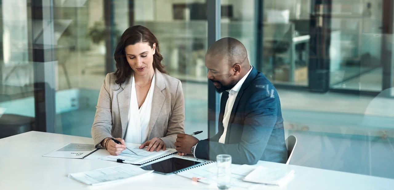 A man and woman looking over papers together at a conference table.
